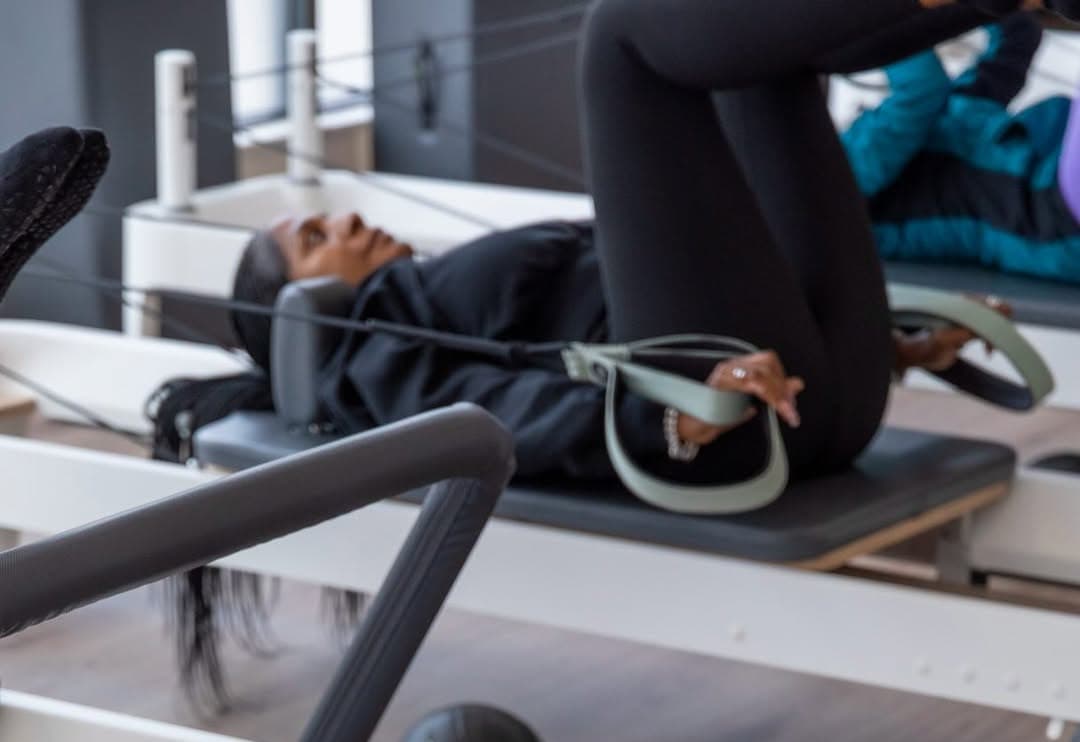 A mother working on a reformer with the loop straps during the Mums and Babies class at Studio Core, a second member on the reformer behind her
