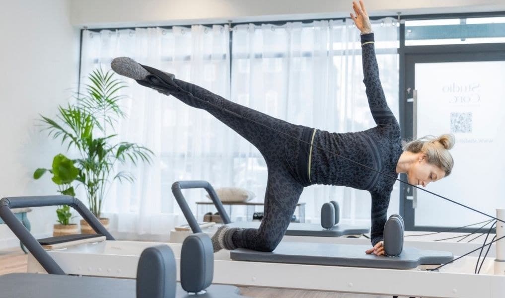 Studio Core member in a kneeling side plank on a reformer with the top leg extended