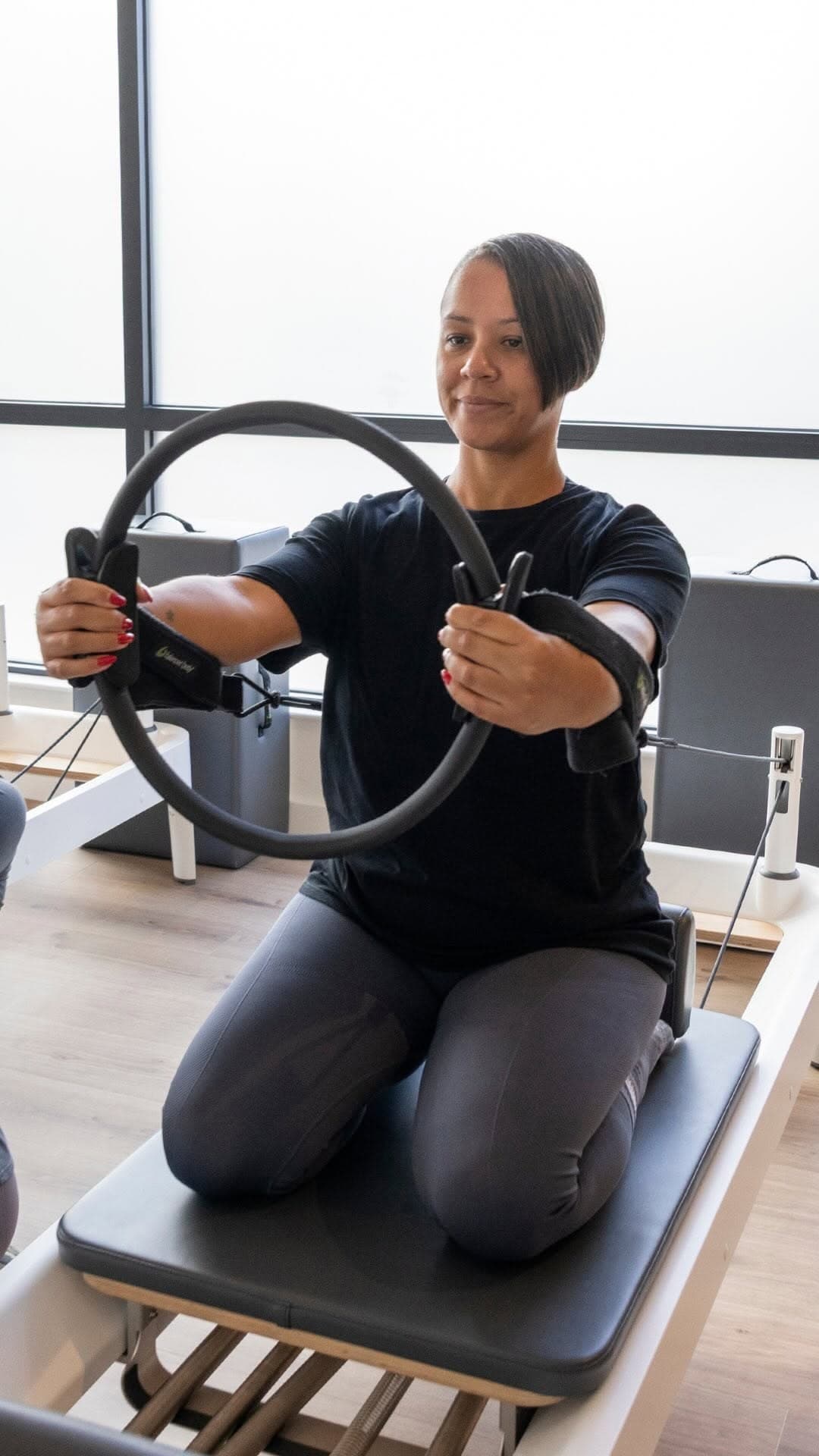 A Studio Core member kneeling upright on a reformer, pressing a Pilates ring, in a private session